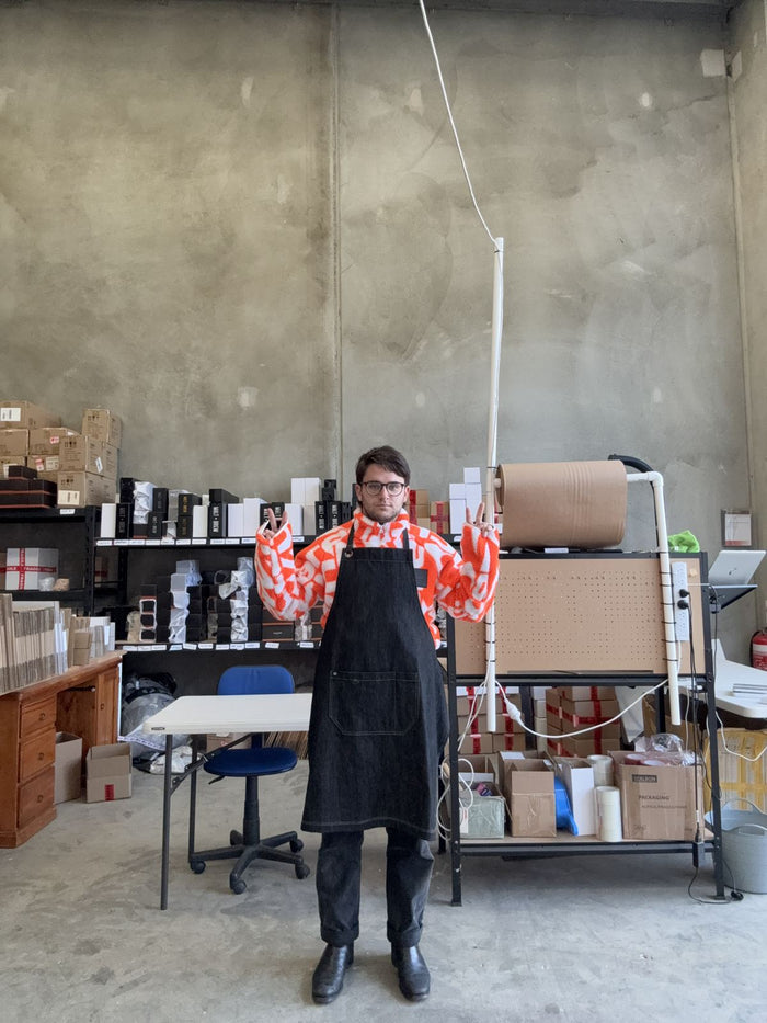 Thomas in an apron and a loud shirt, ready to pour candles, May 2025